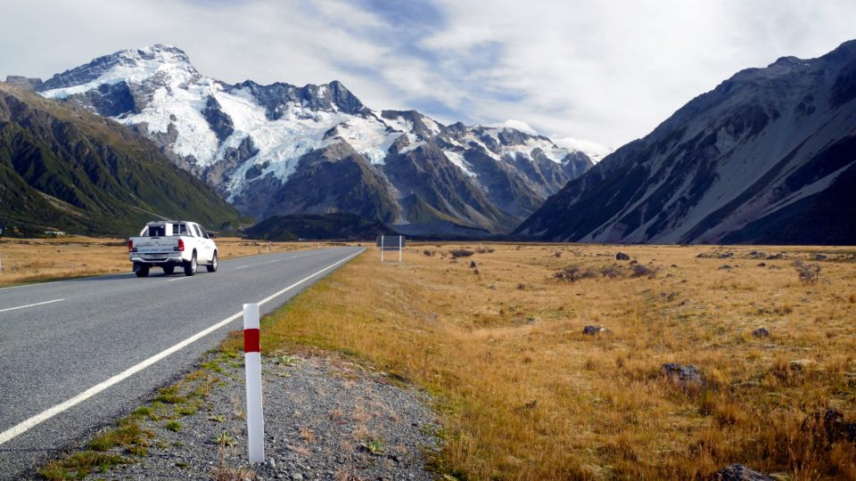 Auto recorriendo una carretera con montañas nevadas al fondo